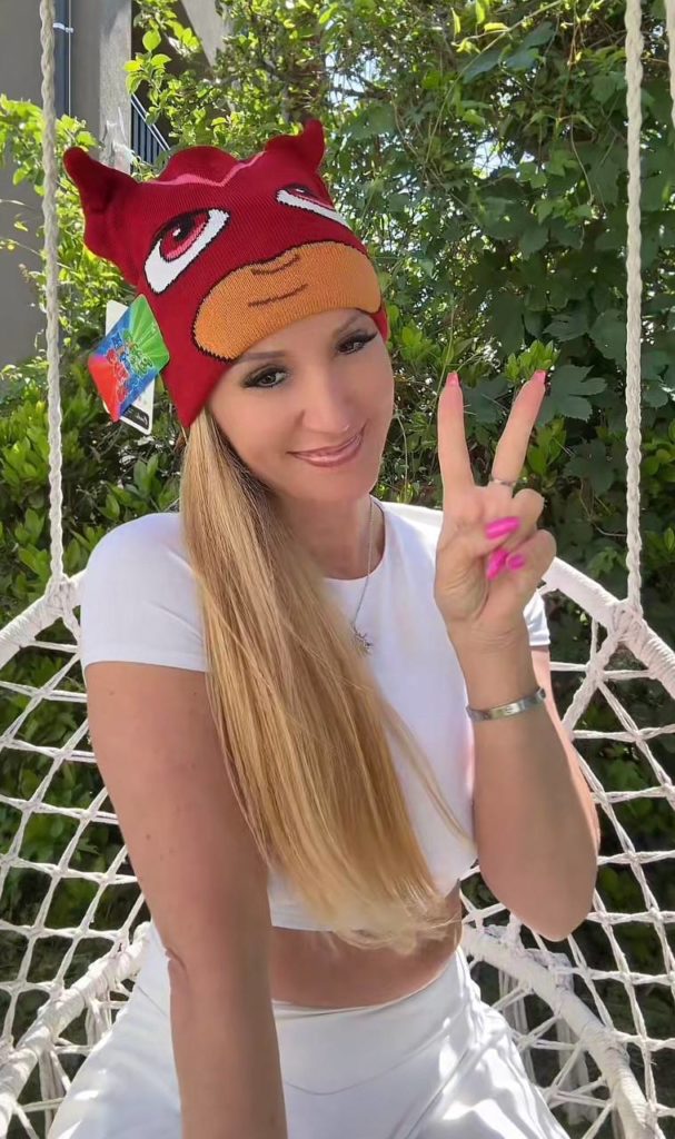 Frau mit bunter Mütze zeigt Friedenszeichen im Garten.