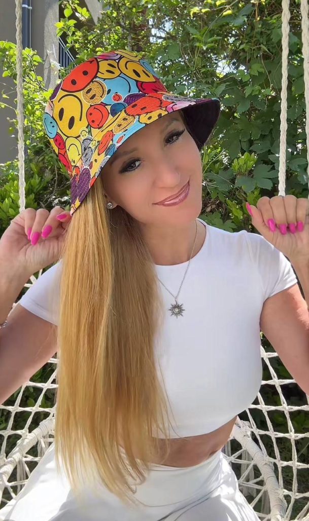 Frau mit buntem Hut und weißem Shirt im Garten.