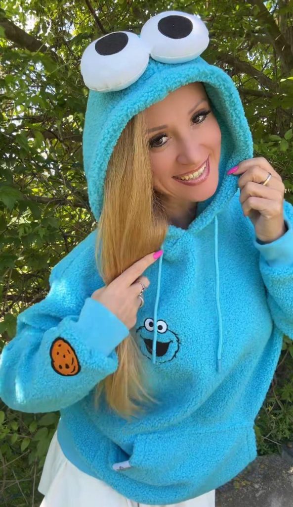 Person im blauen Krümelmonster-Pullover lächelt draußen.